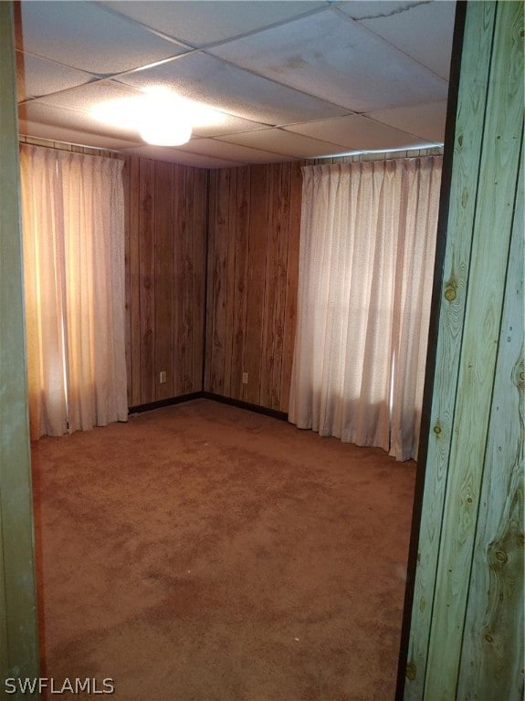 carpeted spare room featuring wood walls and a paneled ceiling