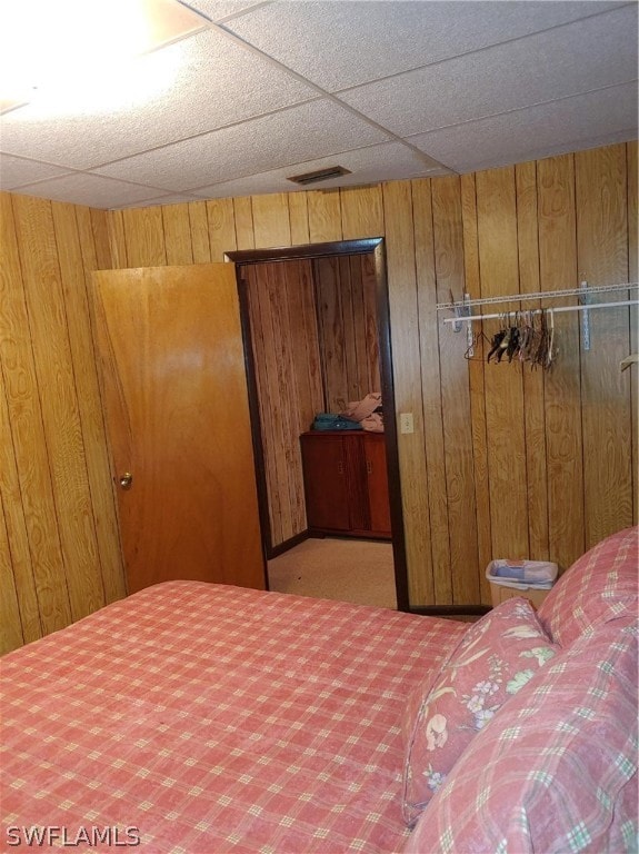 bedroom with a drop ceiling, a closet, carpet floors, and wooden walls