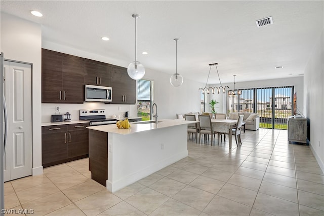 kitchen featuring light tile flooring, a kitchen island with sink, appliances with stainless steel finishes, sink, and dark brown cabinets