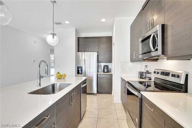 kitchen featuring light tile floors, decorative light fixtures, appliances with stainless steel finishes, dark brown cabinetry, and sink