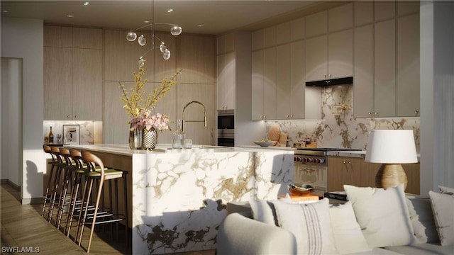 kitchen with a sink, stainless steel gas cooktop, decorative backsplash, a breakfast bar area, and under cabinet range hood
