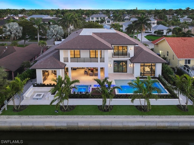 rear view of property with a balcony, a patio area, and a lawn