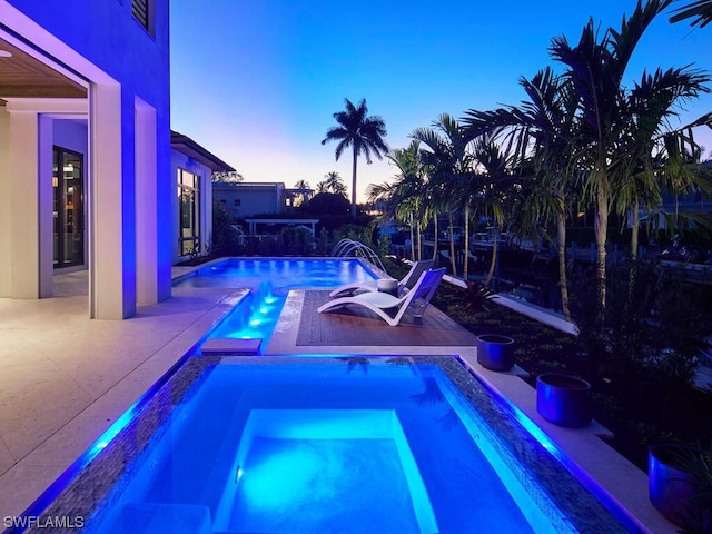 pool at dusk with a patio, pool water feature, and an in ground hot tub