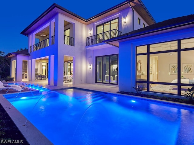 pool at night featuring pool water feature and a patio