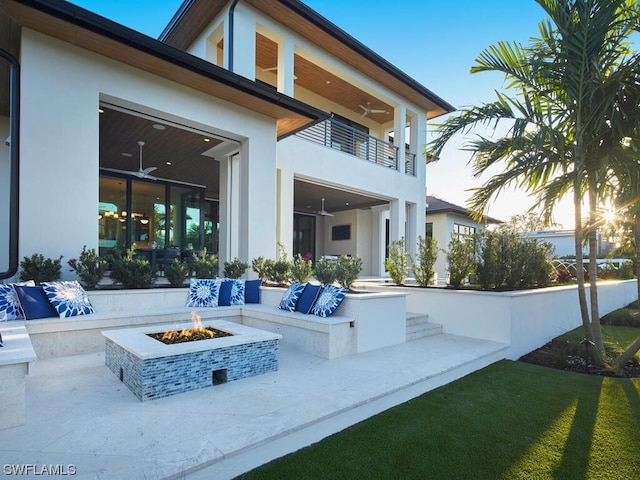 back of property with a balcony, a patio area, ceiling fan, and an outdoor fire pit