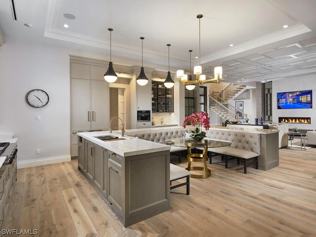 kitchen with a spacious island, sink, hanging light fixtures, gray cabinets, and light hardwood / wood-style floors