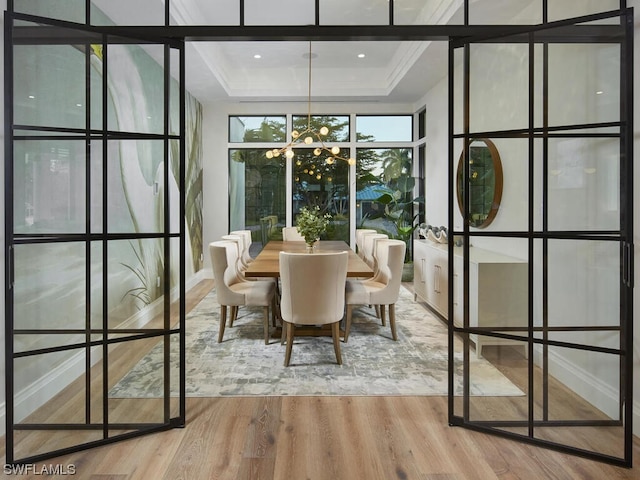 dining space with a tray ceiling, a chandelier, and light wood-type flooring