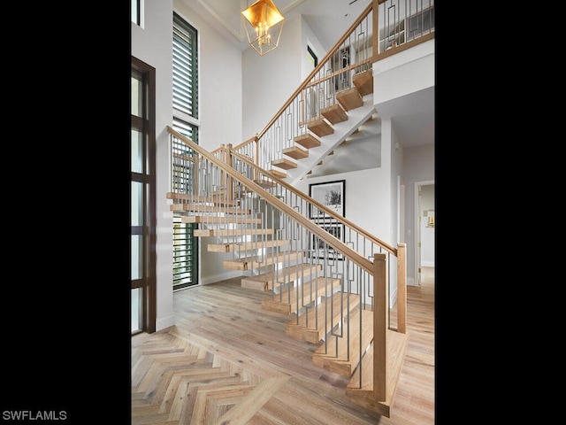 stairway featuring parquet floors, an inviting chandelier, and a high ceiling