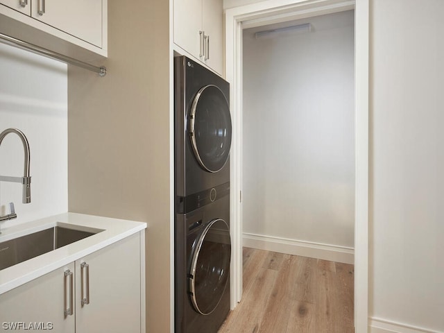 laundry room featuring cabinets, stacked washer and dryer, light hardwood / wood-style floors, and sink