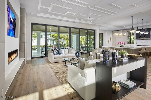 living room with coffered ceiling, light hardwood / wood-style flooring, and a chandelier