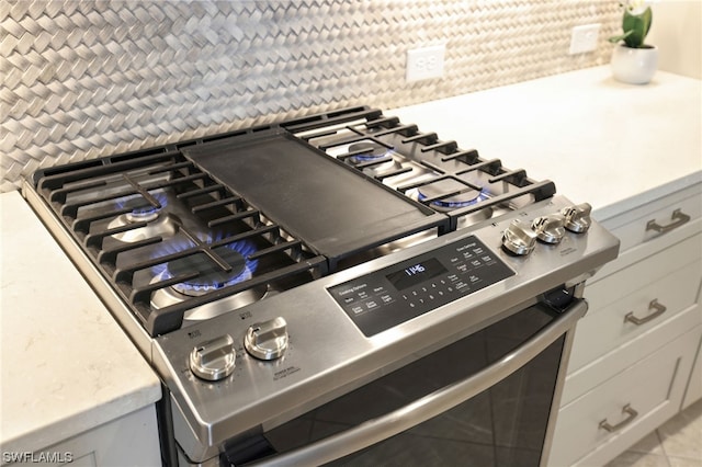 details with light tile patterned floors, stainless steel gas stove, and white cabinetry