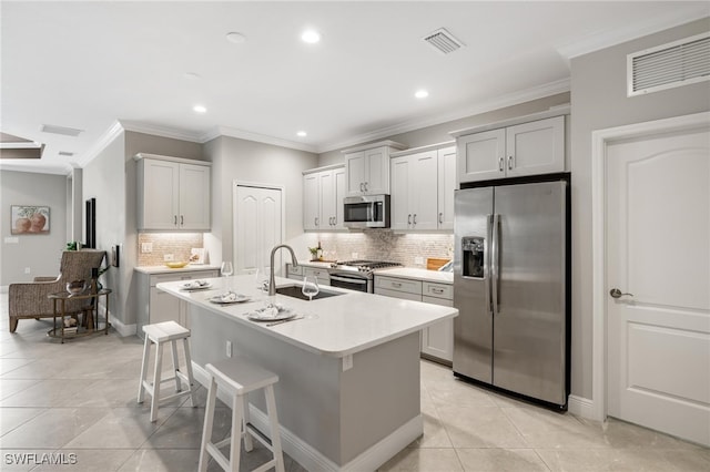 kitchen with an island with sink, stainless steel appliances, ornamental molding, and tasteful backsplash