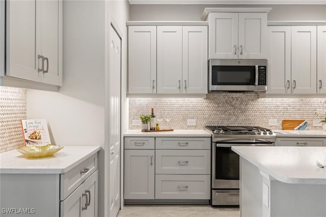 kitchen with gray cabinets, light tile patterned floors, stainless steel appliances, and decorative backsplash