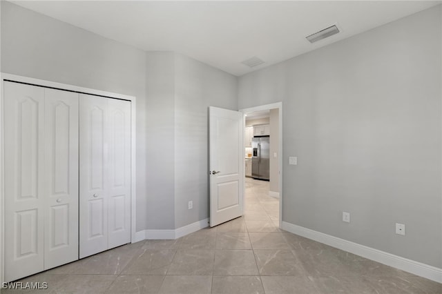 unfurnished bedroom with stainless steel fridge with ice dispenser, light tile patterned flooring, and a closet