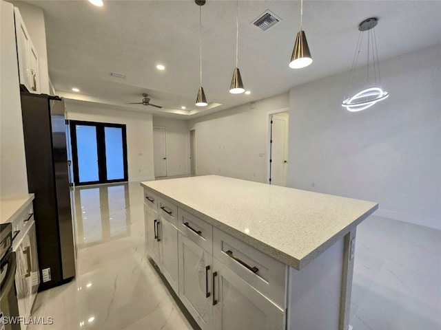 kitchen with ceiling fan, a kitchen island, stainless steel fridge, decorative light fixtures, and white cabinets