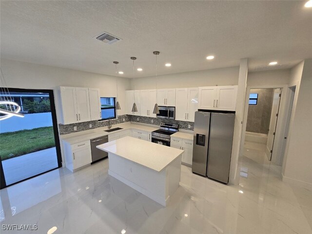 kitchen with white cabinetry, sink, hanging light fixtures, a kitchen island, and appliances with stainless steel finishes