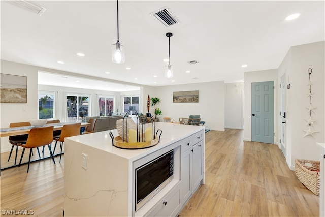 kitchen featuring decorative light fixtures, a kitchen island, white cabinets, stainless steel microwave, and light wood-type flooring