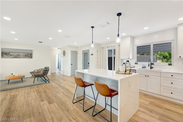 kitchen featuring hanging light fixtures, light hardwood / wood-style floors, sink, white cabinets, and a center island