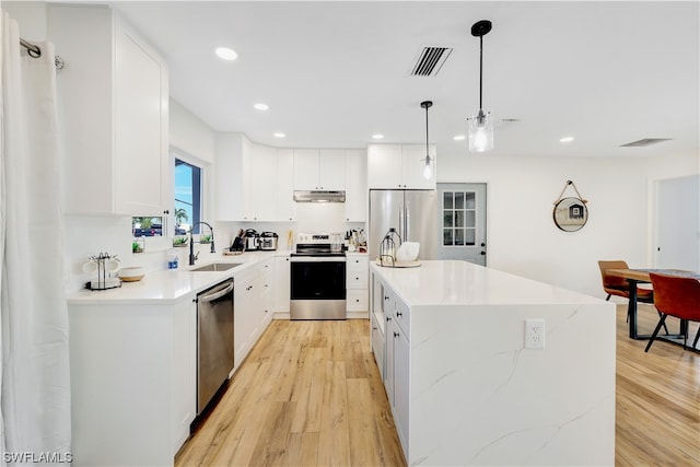 kitchen with a kitchen island, white cabinets, light hardwood / wood-style floors, stainless steel appliances, and decorative light fixtures