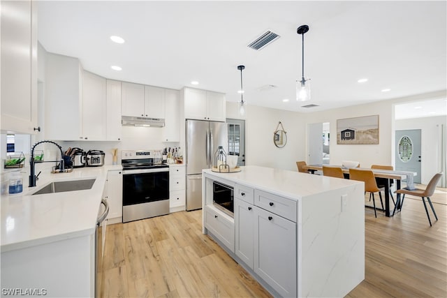 kitchen with decorative light fixtures, white cabinetry, light hardwood / wood-style floors, sink, and stainless steel appliances