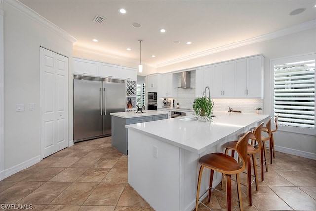 kitchen with pendant lighting, built in appliances, a breakfast bar, wall chimney exhaust hood, and backsplash