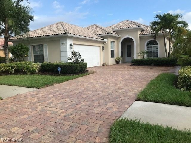 view of front of home featuring an attached garage, stucco siding, decorative driveway, and a tiled roof