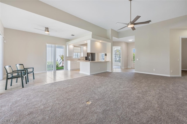 unfurnished living room featuring a ceiling fan, a wealth of natural light, and light colored carpet