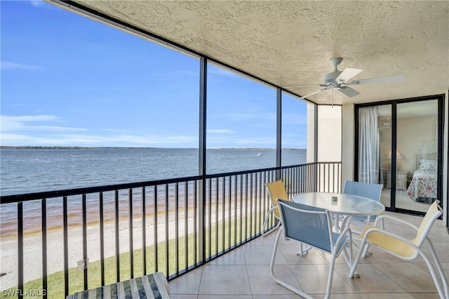 unfurnished sunroom featuring a beach view, ceiling fan, and a water view