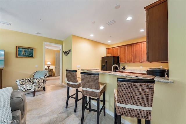 kitchen with light tile floors, kitchen peninsula, light stone counters, and black fridge