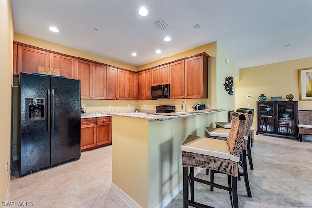 kitchen featuring a breakfast bar area, light tile floors, black appliances, and light stone countertops