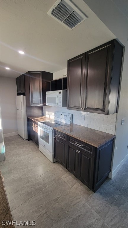 kitchen with white appliances, light tile floors, dark stone counters, backsplash, and dark brown cabinetry