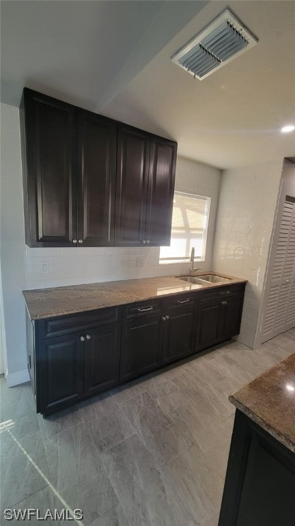 kitchen with light tile flooring, backsplash, dark stone counters, and sink