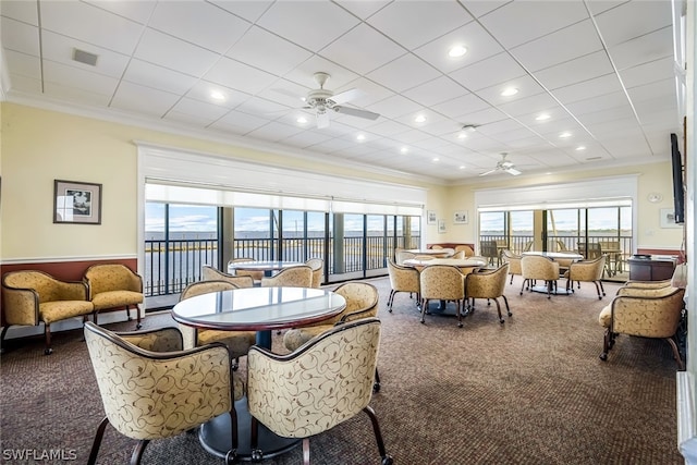 carpeted dining space with ceiling fan, a water view, and ornamental molding