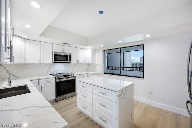 kitchen with light stone counters, stainless steel appliances, sink, white cabinets, and light hardwood / wood-style floors