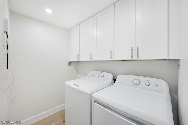 clothes washing area with washing machine and clothes dryer, light hardwood / wood-style flooring, and cabinets