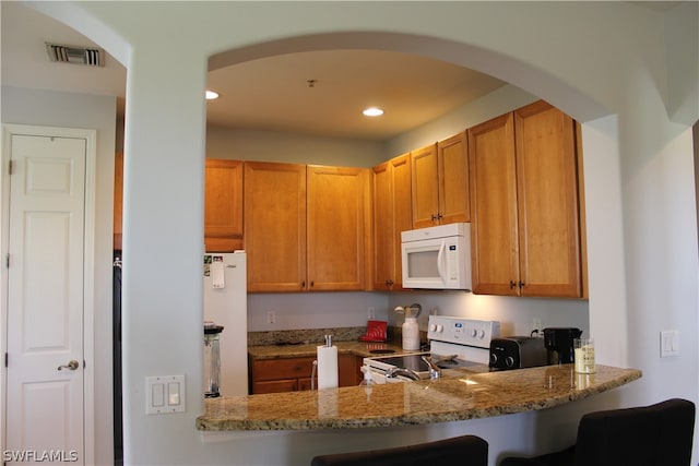 kitchen featuring light stone countertops, a kitchen breakfast bar, white appliances, and kitchen peninsula