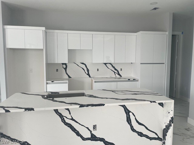 kitchen with white cabinets, backsplash, light stone counters, and a kitchen island