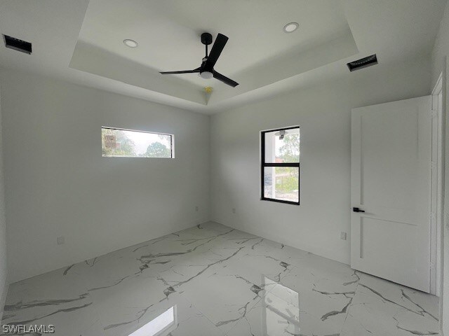 empty room with tile patterned floors, ceiling fan, and a tray ceiling