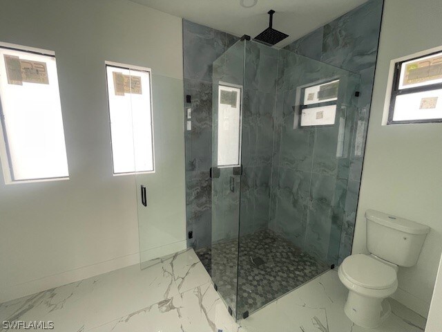 bathroom with a shower with door, toilet, tile patterned floors, and a wealth of natural light