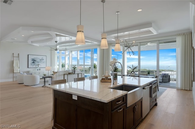 kitchen with pendant lighting, sink, light wood-type flooring, light stone countertops, and dark brown cabinets