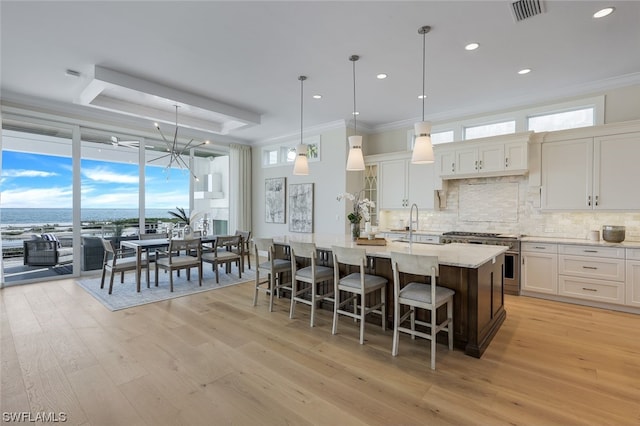 kitchen with high end range, a center island with sink, light hardwood / wood-style flooring, and hanging light fixtures