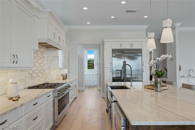 kitchen featuring white cabinetry, premium appliances, light hardwood / wood-style flooring, a large island with sink, and decorative light fixtures