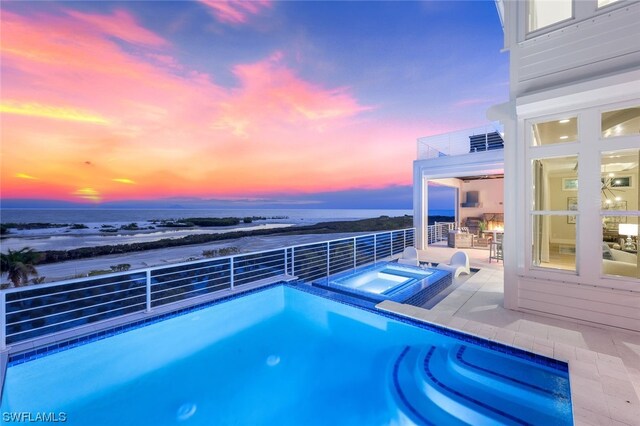 pool at dusk featuring an in ground hot tub and a patio area