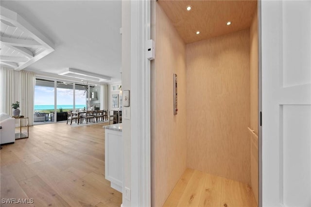 hallway featuring a water view, elevator, light wood-style floors, and recessed lighting