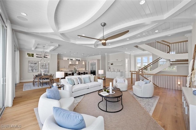 living room featuring a ceiling fan, beam ceiling, light wood finished floors, and stairs