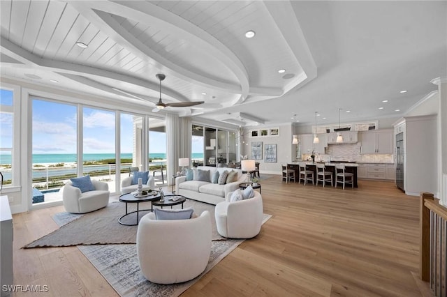 living room featuring a ceiling fan, beamed ceiling, a water view, crown molding, and light wood-style floors