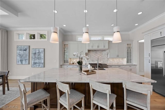 kitchen featuring hanging light fixtures, a breakfast bar, a large island with sink, and built in fridge