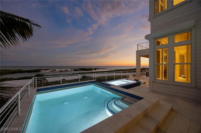 pool at dusk featuring an in ground hot tub and a water view