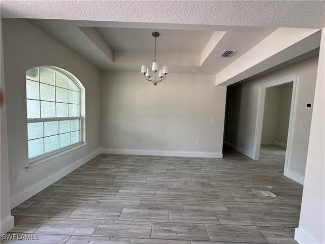 unfurnished room featuring a textured ceiling, a raised ceiling, a chandelier, and light hardwood / wood-style flooring