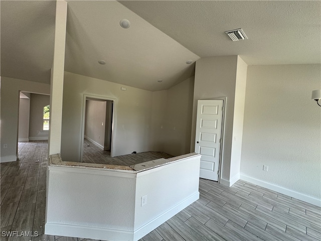 kitchen featuring a textured ceiling, lofted ceiling, light wood-type flooring, and kitchen peninsula